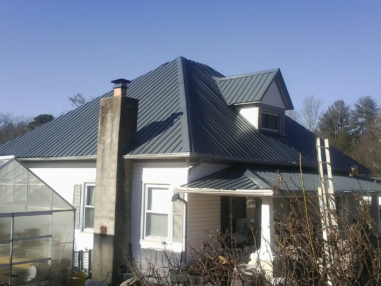 Dark blue standing seam metal roof on a white farmhouse with dormer — Slate & Tile Roof Repair by Roofing Brothers in Stone Creek