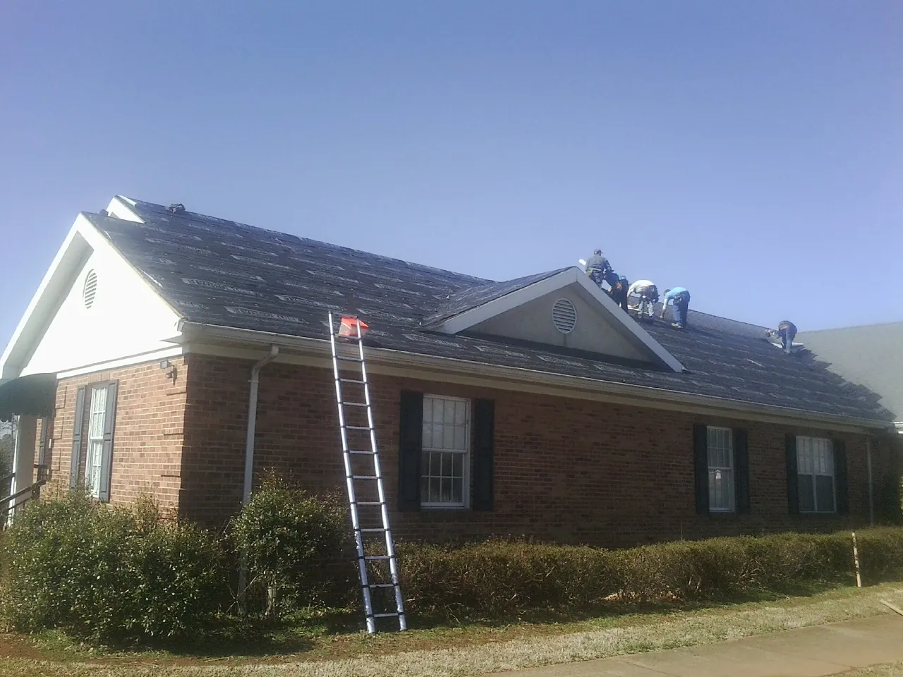 Crew tearing shingles off a brick ranch roof with a ladder set — Metal Roof Repair work by our crew in Stone Creek