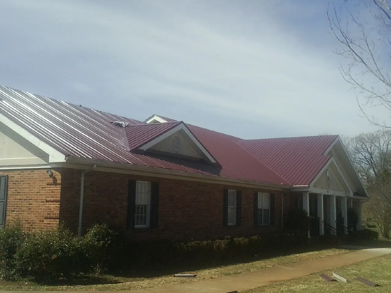 Red metal roof with gabled entries on a long brick building, from a Hail Damage Roof Repair job in Stone Creek