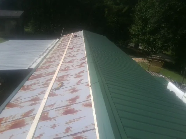 Old rusted panels beside newly installed green metal roofing — Wind Damage Roof Repair by Roofing Brothers in Stone Creek
