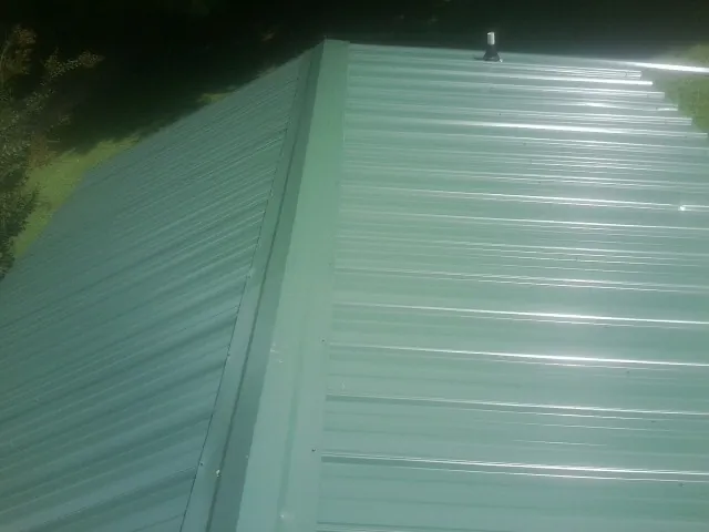 New green metal panels meeting at the ridge of a roof — Flat Roof Repair work by our crew in Stone Creek