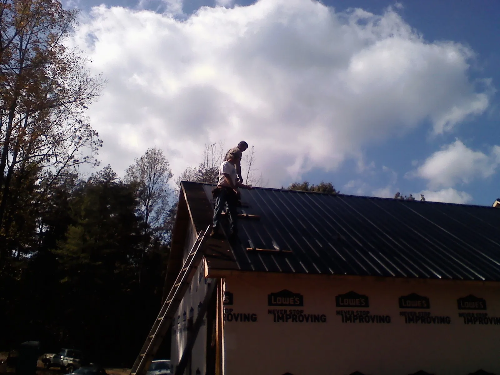 Roofer fastening dark metal panels high against a cloudy sky, from a Roof Inspection job in Stone Creek