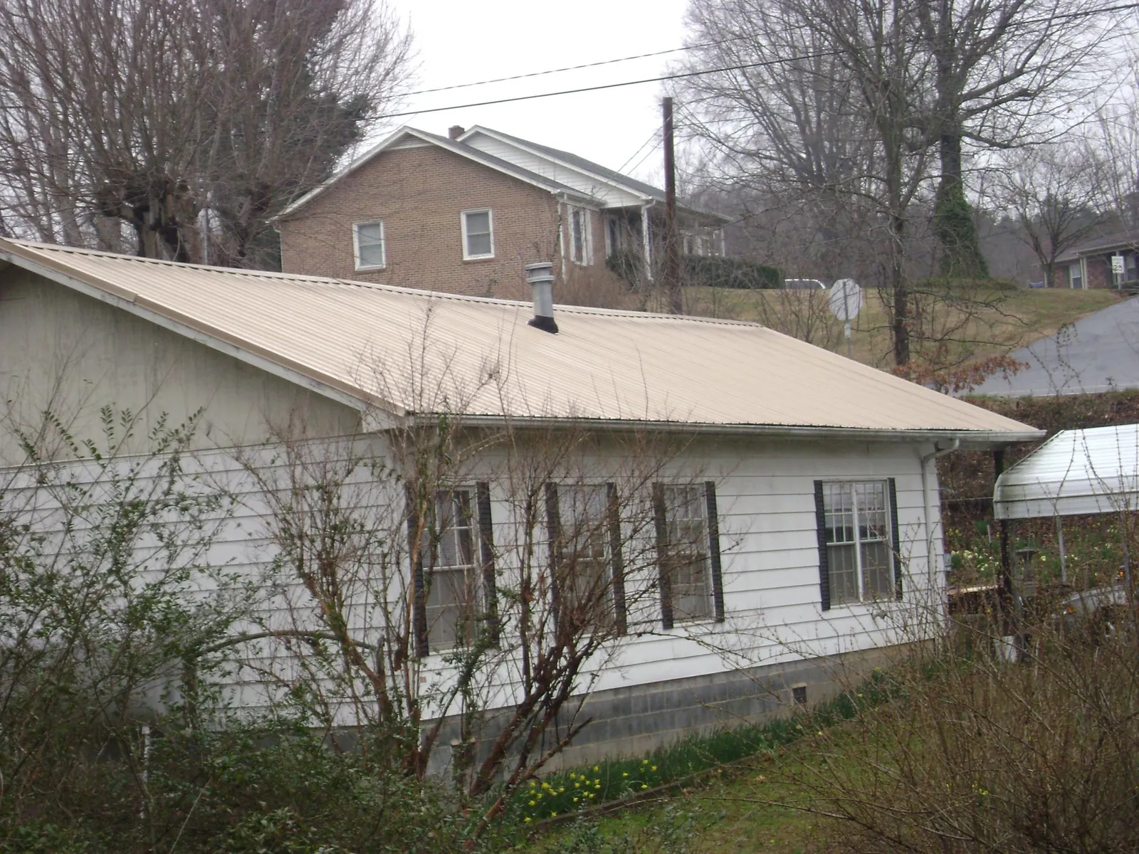 Tan metal roof on a white sided house set into a hillside — Commercial Roofing by Roofing Brothers in Stone Creek