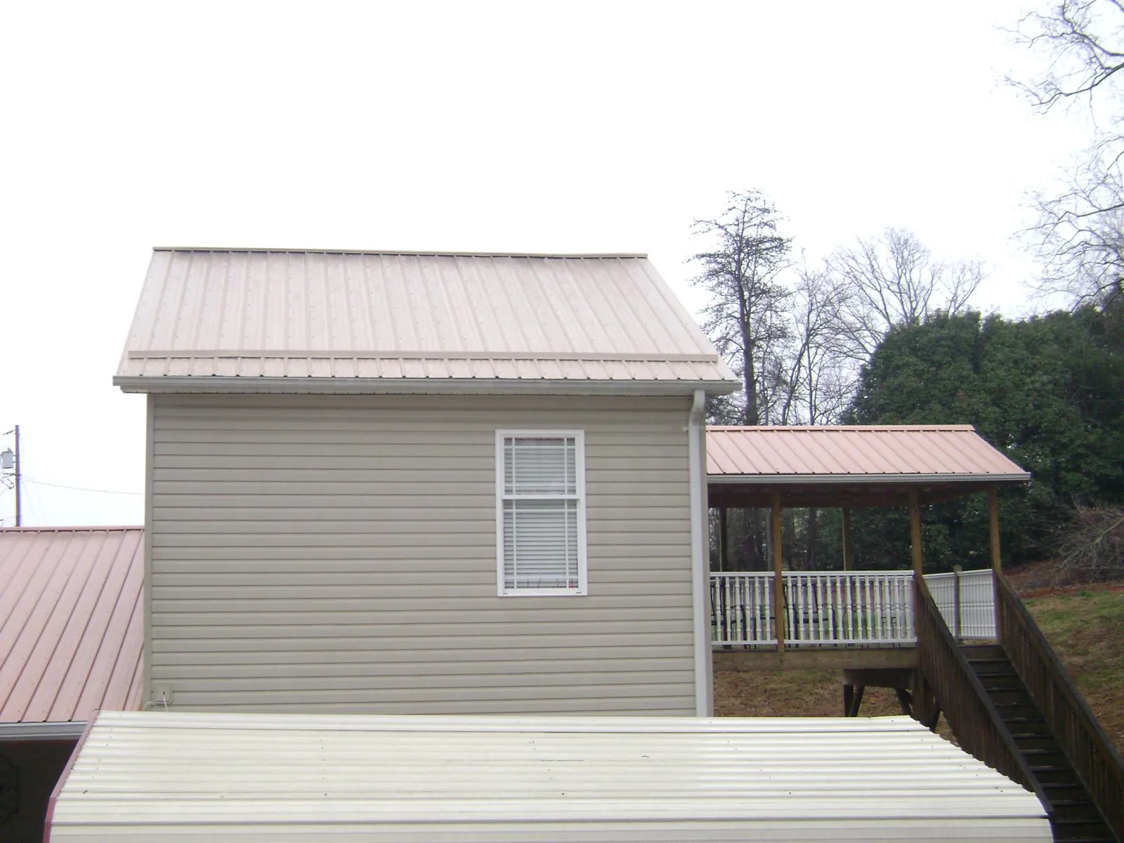 Tan metal roofs on a two story addition and attached porch, from a Roof Replacement job in Stone Creek